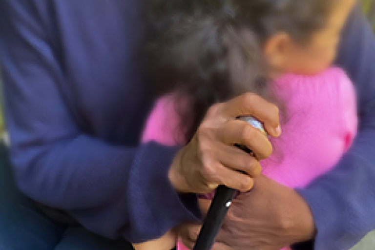 Plano aproximado de uma avó negra a segurar uma bengala e a abraçar uma menina