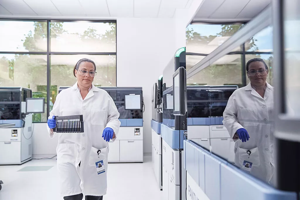 Técnico de laboratório a transportar um tabuleiro de frascos num laboratório
