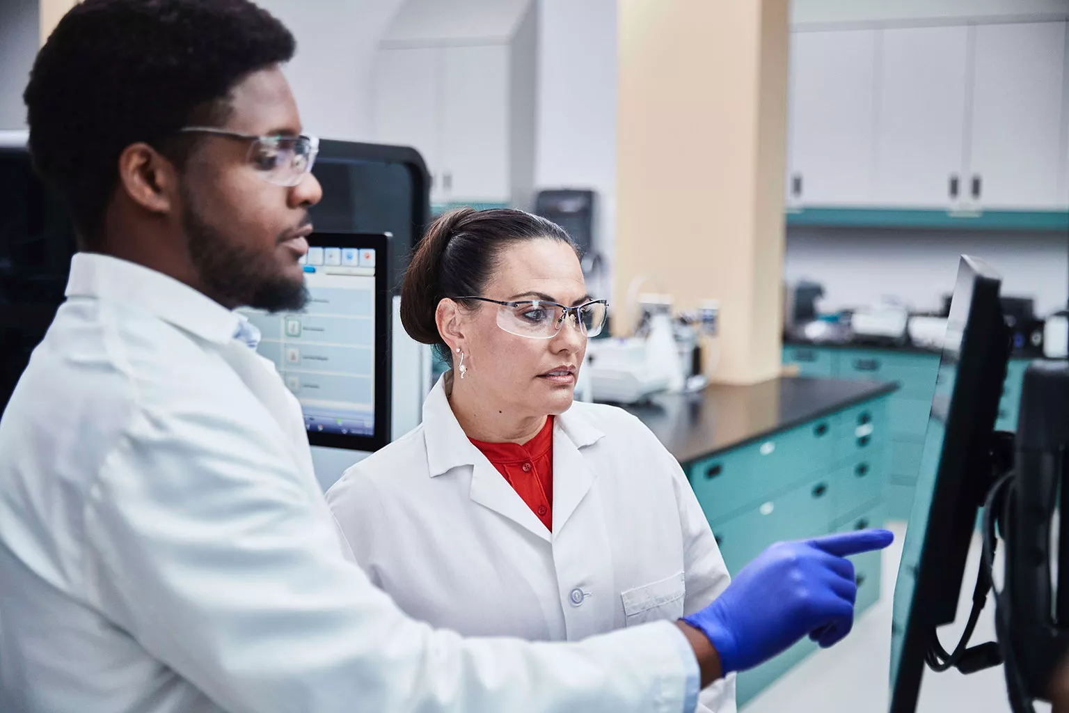 Técnico de laboratório a olhar e a apontar para um monitor no laboratório