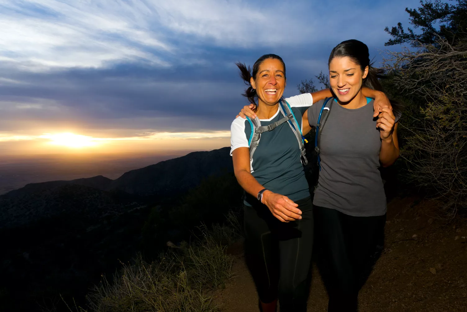 Duas mulheres a caminhar numa colina no por do sol.